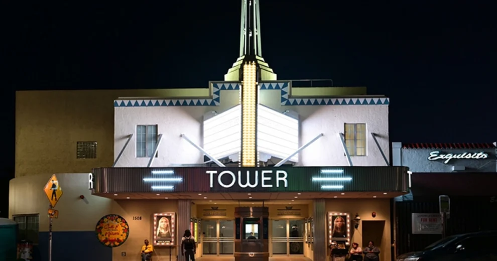 Nighttime exterior of the Tower Theater in Little Havana, Miami. The historic Art Deco-style façade is illuminated, highlighting the vertical tower and large “TOWER” marquee, with people gathered near the theater entrance.