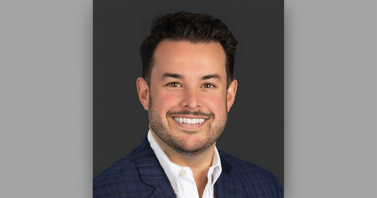 Professional headshot of Branden Lopez smiling and wearing a navy plaid suit jacket and white dress shirt against a dark gray background.