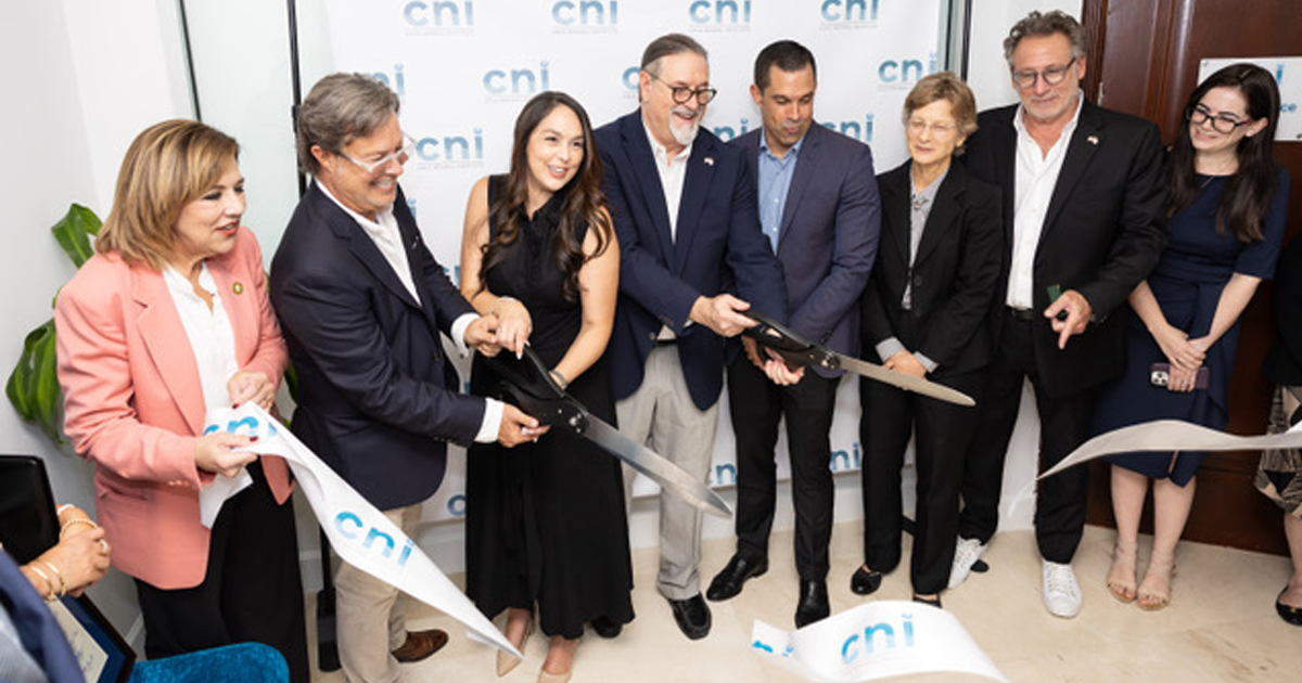 A group of adults participates in a ribbon-cutting ceremony in front of a CNI-branded backdrop, holding large ceremonial scissors.