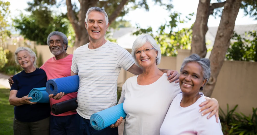 A diverse group of five older adults smiling outdoors while holding rolled exercise mats, promoting fitness, wellness, and active aging.