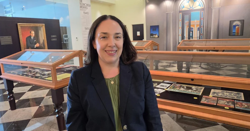 Amanda Moreno-Schroeder, Librarian Associate Professor, Esperanza Bravo de Varona Chair and Director of the Cuban Heritage Collection, stands inside a museum exhibit featuring historical Cuban memorabilia, photographs and archival materials.