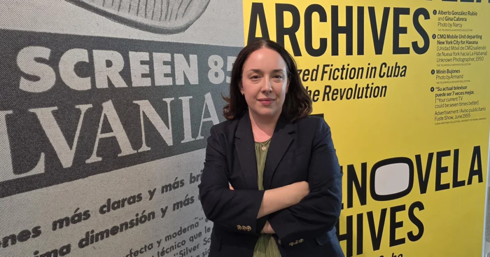 Amanda Moreno-Schroeder, Librarian Associate Professor, Esperanza Bravo de Varona Chair and Director of the Cuban Heritage Collection, stands with her arms crossed in front of a large exhibit graphic highlighting Cuban archives, vintage publications and Spanish-language materials.