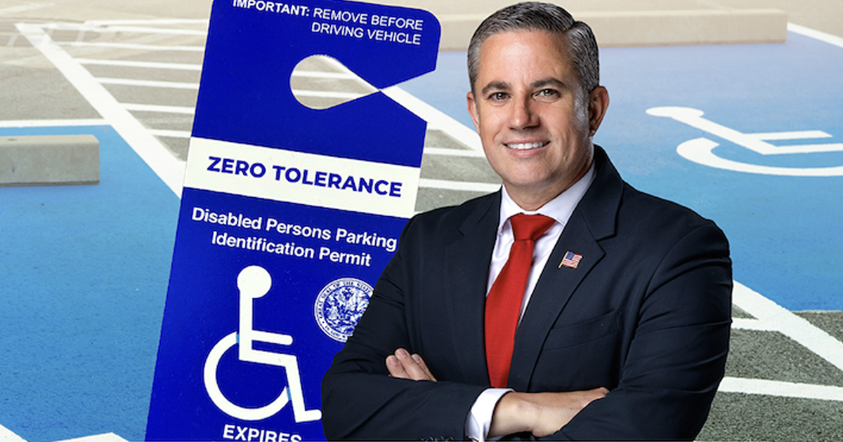 Miami-Dade County Tax Collector Dariel Fernandez stands with his arms crossed in front of a disabled parking space and a large blue sign promoting zero tolerance for misuse of disabled persons parking identification permits.