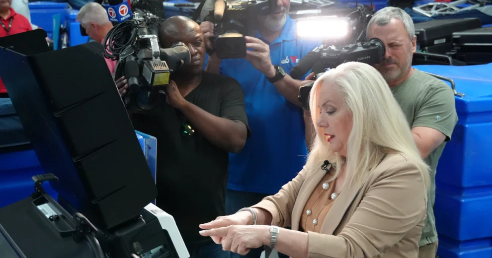 La supervisora ​​de elecciones del condado de Miami-Dade, Alina García, opera una máquina de votación mientras las cámaras de noticias de televisión graban la demostración.