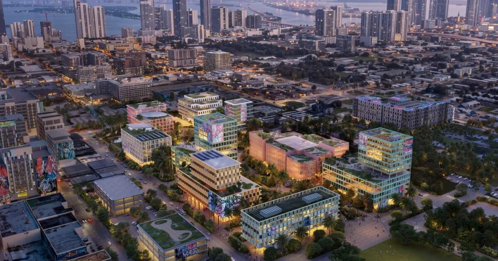 La Universidad Carnegie Mellon de Miami transformará Wynwood con un campus de 2 mil millones de dólares respaldado por Ken Griffin 1 Representación aérea de un gran complejo de uso mixto en Miami, que incluye modernos edificios de oficinas y residenciales, espacios públicos ajardinados y coloridos murales, con los rascacielos del centro de Miami y el paseo marítimo al fondo.