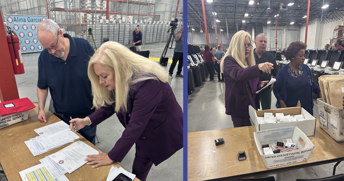Miami-Dade County election officials inspect paperwork and election materials at a warehouse facility. Supervisor of Elections Alina Garcia&rsquo;s banner is visible in the background as staff review documents and equipment.