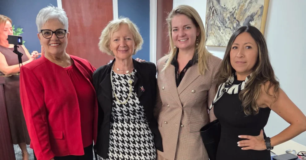 Four women pose together indoors, smiling at the camera.