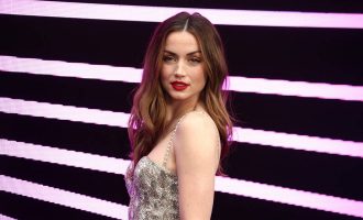 Ana de Armas in a silver gown standing in front of a black and white striped background.