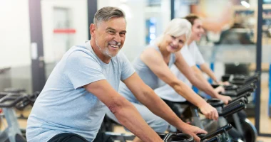 A group of older adults exercising on stationary bikes at a gym, smiling and participating in a fitness workout.