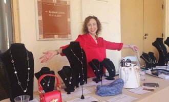 Una mujer vestida de rojo de Charity Connections está parada junto a una mesa llena de varios bolsos y carteras.