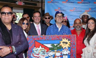Un grupo de asistentes posa junto en un evento de "Cuba Nostalgia", sonriendo frente a un telón de fondo con la marca mientras sostienen una colorida obra de arte con motivos de inspiración cubana.