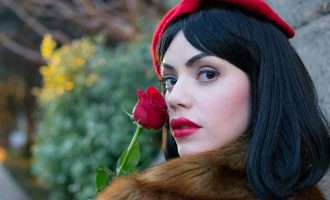 Una mujer con cabello negro y lápiz labial rojo sostiene con gracia una rosa vibrante.