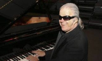 Pianist Mike Gerber sitting in front of a piano with a black suit.