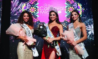 Tres ganadoras del concurso se paran en el escenario frente a un colorido fondo de “Miss Carnaval Miami” con gráficos de fuegos artificiales.