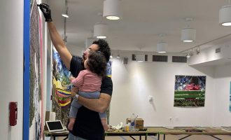 William Osorio painting on a canvas while holding his daughter.