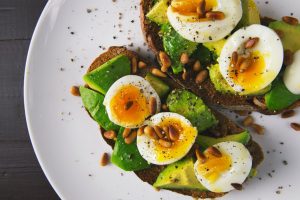Two slices of bread with avocado, boiled eggs, and hemp seeds sprinkled on top.