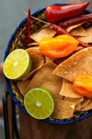 A bowl of tortilla chips with lime and chillis.