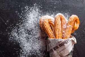 Delicious-looking churros wrapped in a newspaper, with powdered sugar sprinkled on them.