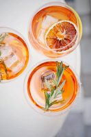 An orange-flavored cocktail with ice cubes, orange slices, and herbs.