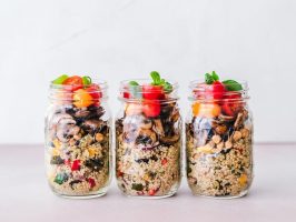 A row of pre-prepared healthy salad jars with quinoa and vegetables.