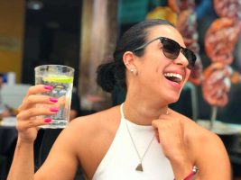 A woman smiles wide while holding the perfect drink in her hand.